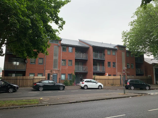 Modern brick apartments beside a tree-lined street in Urmston
