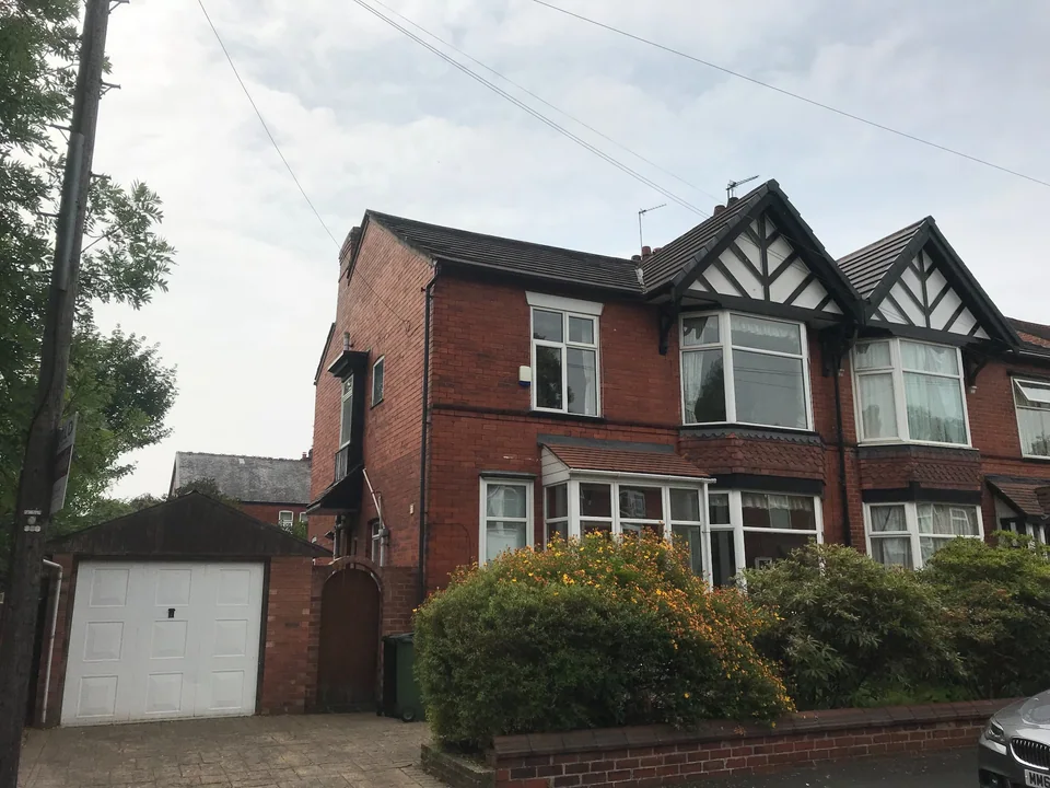Red-brick bay-fronted house with decorative gables, a front garden and an adjoining garage