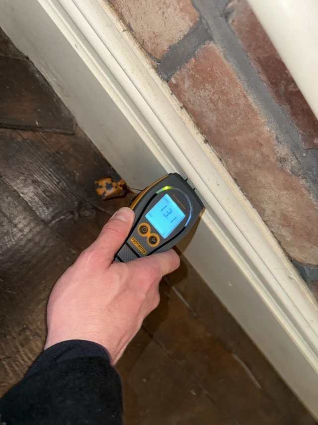 Hand-held moisture meter being used beside an exposed masonry reveal